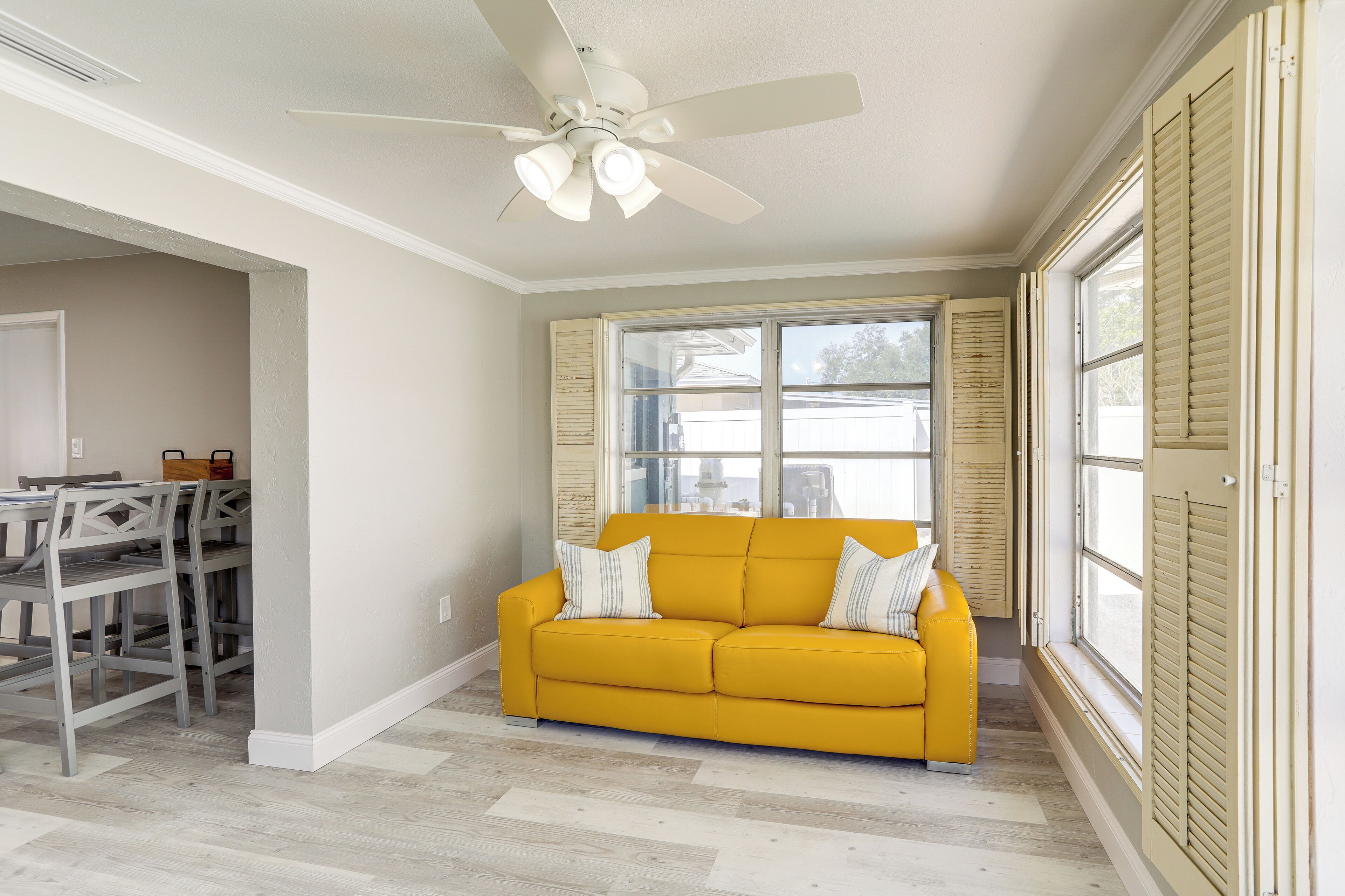 A living room with a yellow sofa, a ceiling fan, and a dining area with a table and chairs.
