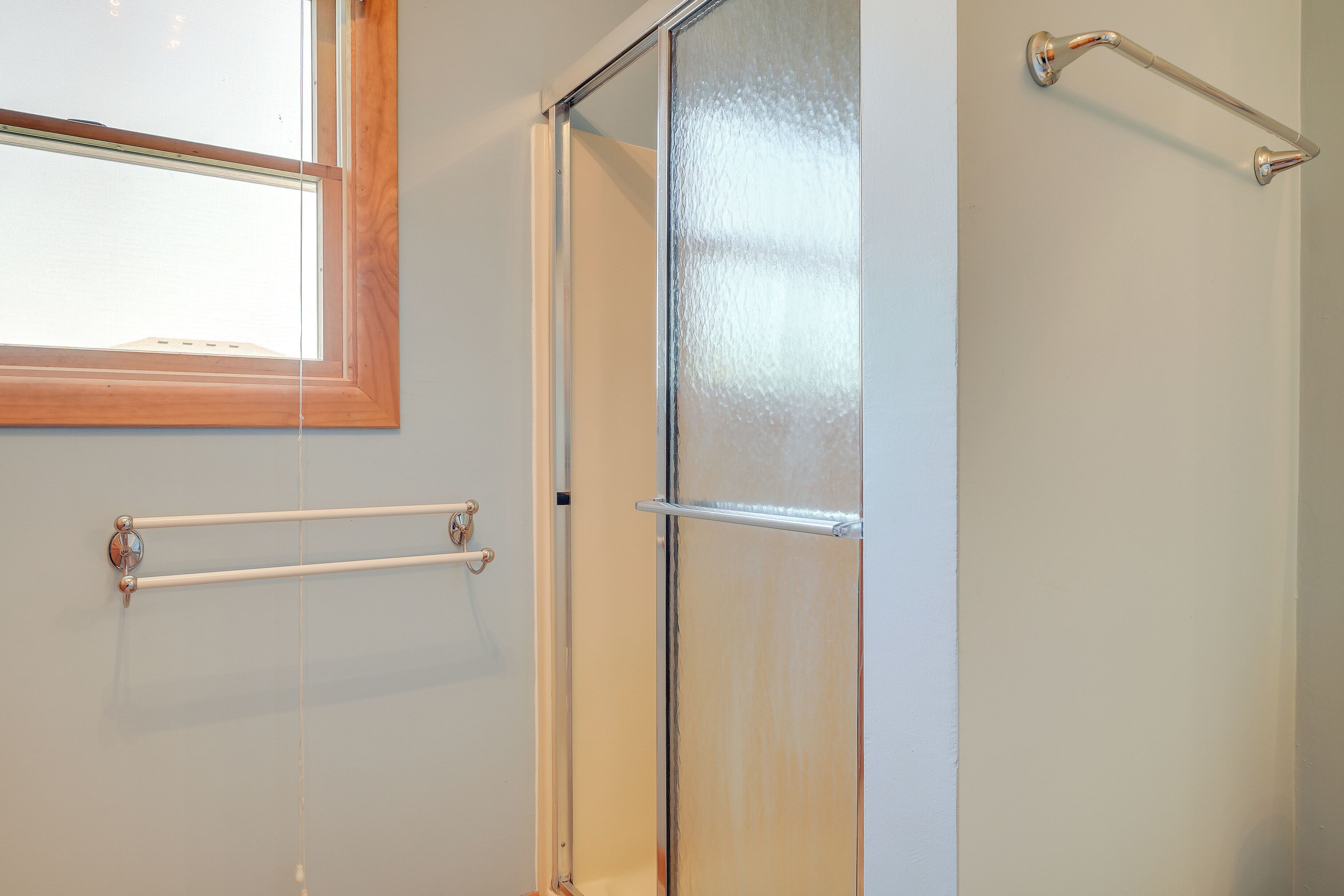 Une salle de bain avec une porte de douche en verre, un porte-serviettes et une fenêtre.