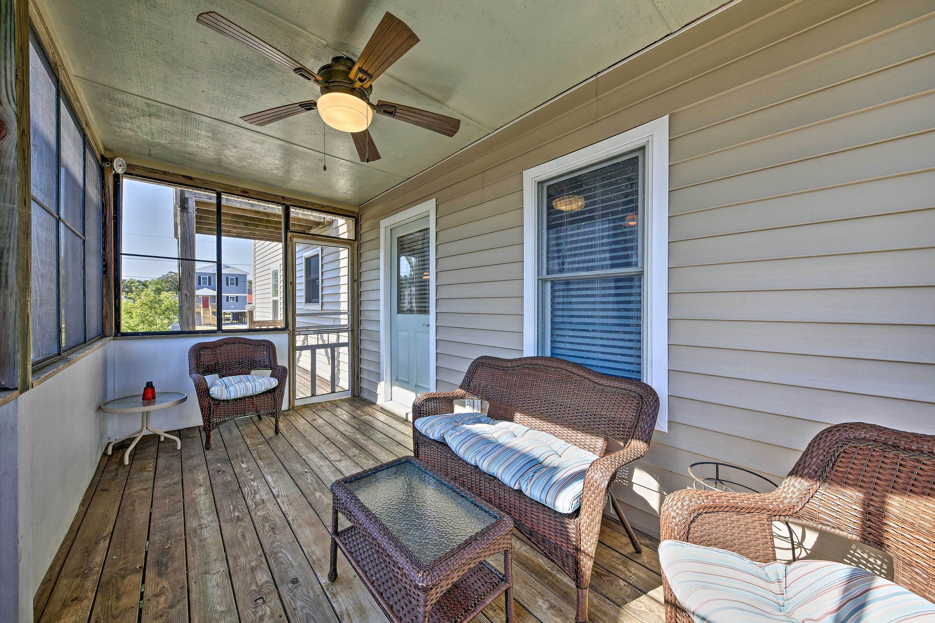 A covered porch with wicker furniture, a ceiling fan, and large windows.