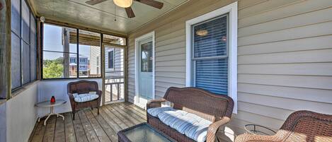 A covered porch with wicker furniture, a ceiling fan, and large windows.