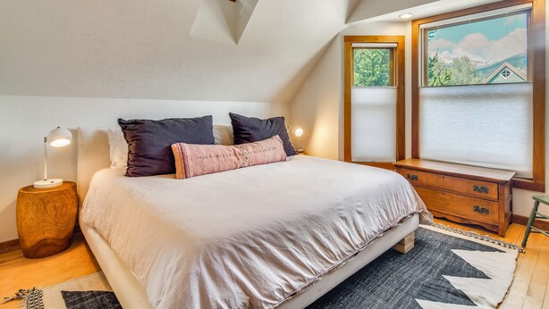 Une chambre à coucher comprenant un lit, une lampe de chevet, une table de chevet en bois, une commode et une fenêtre avec des stores.
