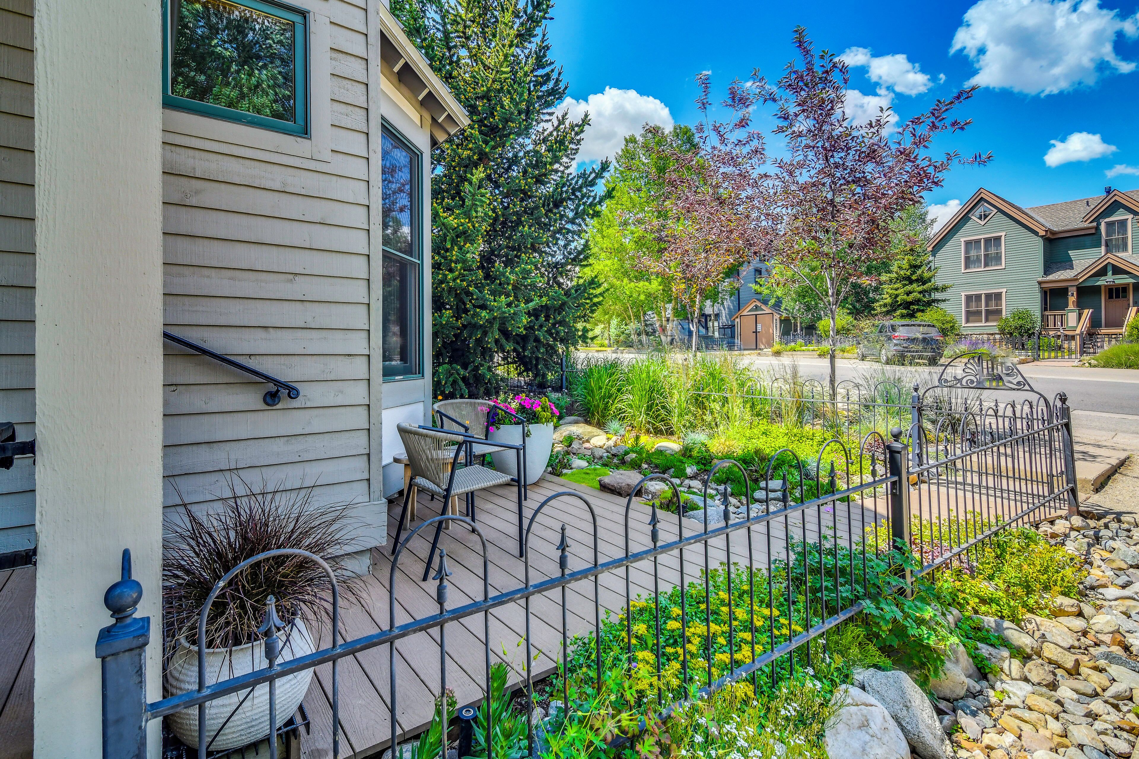 A residential area with a house featuring a porch with outdoor furniture and a garden with various plants and a metal fence.