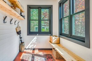 A hallway with a window, a shoe rack, a woven basket, and a rug.