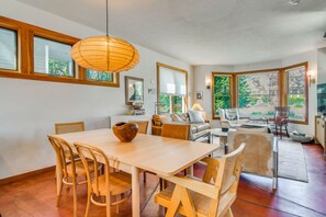 Zona pranzo con tavolo e sedie in legno, lampadario a sospensione e ampie finestre con vista sul verde.