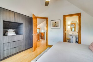 A bedroom with a bed, a wardrobe, a bathroom with a sink and mirror, and a hallway leading to another room.