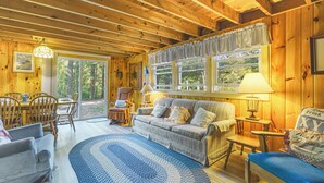 Ein gemütliches Blockhäuschen-Interieur mit Holzwänden, einem Essbereich, einer Couch und einem Fenster mit Vorhängen.
