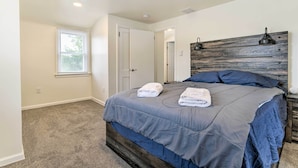 Quarto com cama grande, cabeceira de madeira, janela com persianas e uma porta.