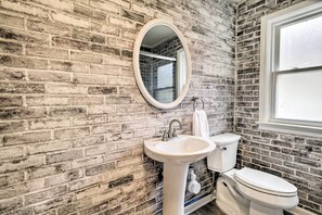 A bathroom with a brick wall, a white sink, a toilet, and a window. - Pet-friendly York Home w/ Patio & Yard (York)
