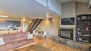 A spacious living area with a wooden floor, a fireplace, a sofa, and a dining table with chairs. - Whitefish Mountain Ski-in/out Condo w/ Views! (Whitefish)