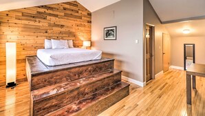 A bedroom with a wooden wall, a bed, a staircase, and a door. - Whitefish Mountain Ski-in/out Condo w/ Views! (Whitefish)