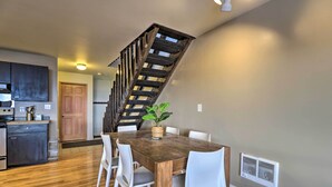 A dining area with a wooden table, white chairs, and a potted plant. A staircase with wooden railings leads to another room. - Whitefish Mountain Ski-in/out Condo w/ Views! (Whitefish)