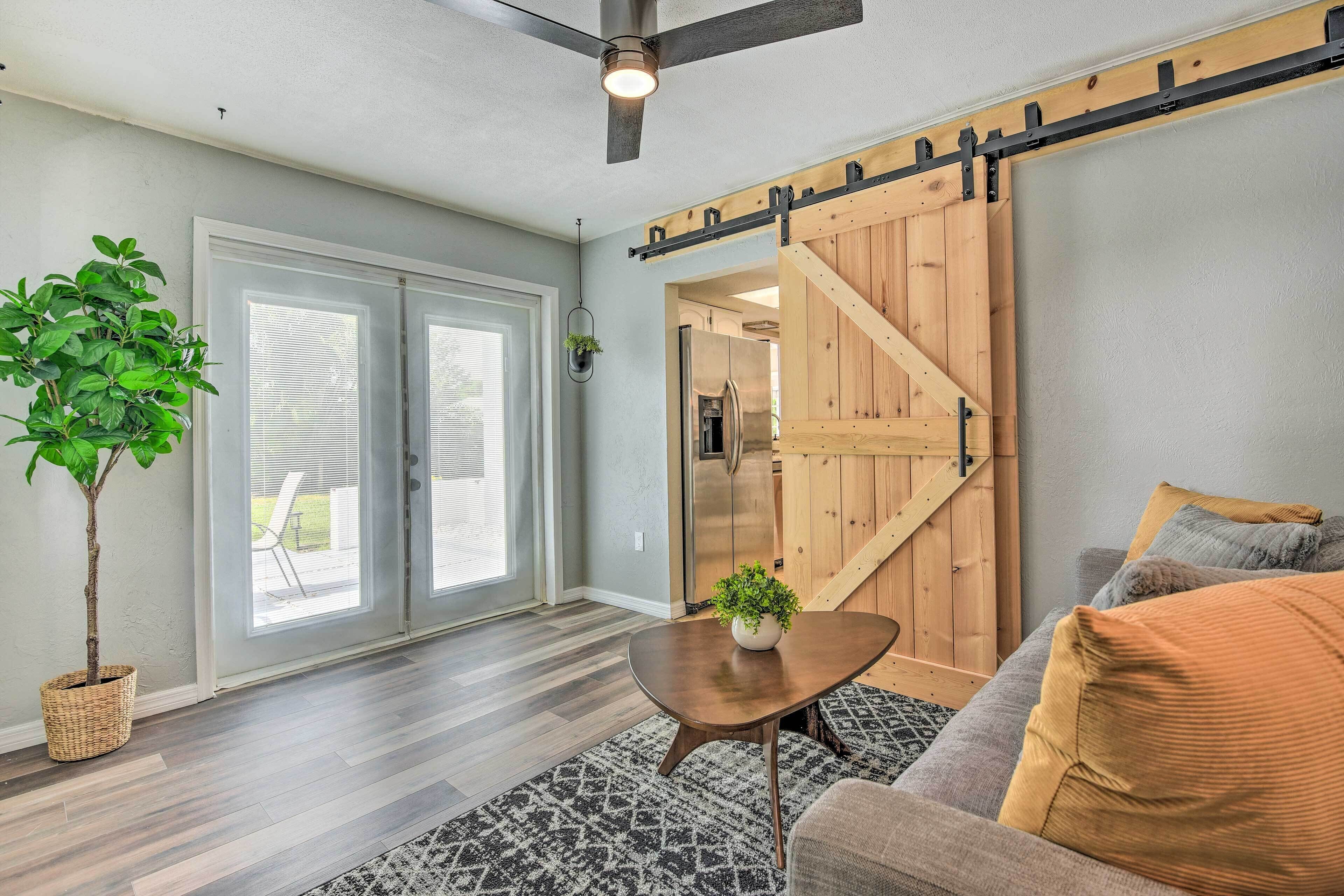 Un salon doté d’une porte coulissante de style grange, d’un ventilateur de plafond, d’une plante en pot, d’un canapé avec des coussins et d’un tapis à motifs.