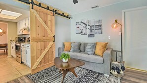 A cozy living room with a sliding barn door, a gray sofa with cushions, a coffee table with a plant, and artwork on the wall. - 8 Mi to Beaches: Bradenton Home w/ Poolside Oasis! (Bradenton)