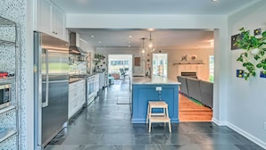 A modern kitchen with a large island, stainless steel appliances, and a wooden stool. - Peaceful Southern Pines Home w/ Pool + Yard! (Southern Pines)