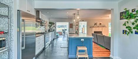 A modern kitchen with a large island, stainless steel appliances, and a wooden stool.