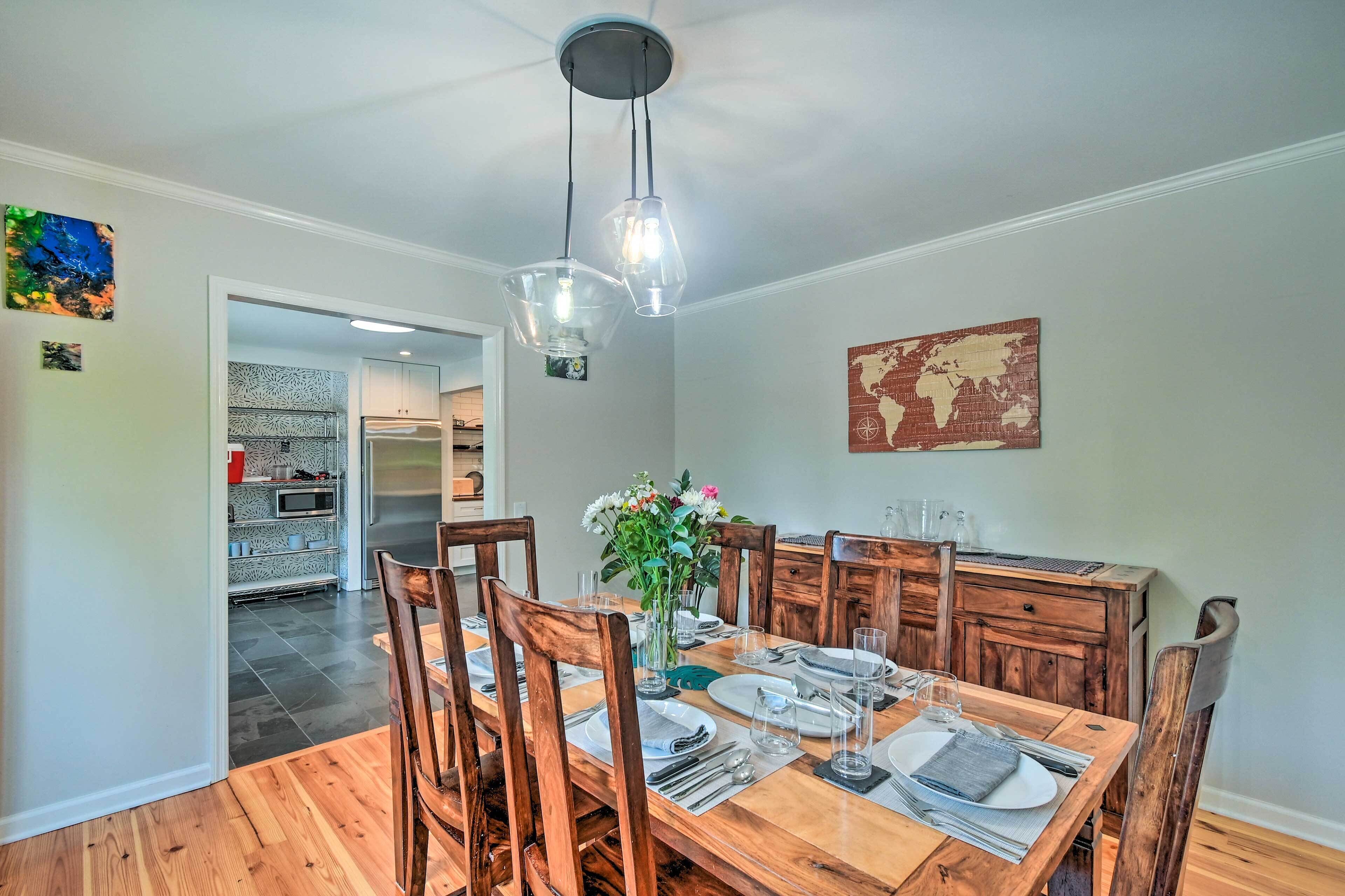 A dining room with a wooden table set for six, surrounded by wooden chairs. A vase with flowers is on the table, and a world map hangs on the wall.