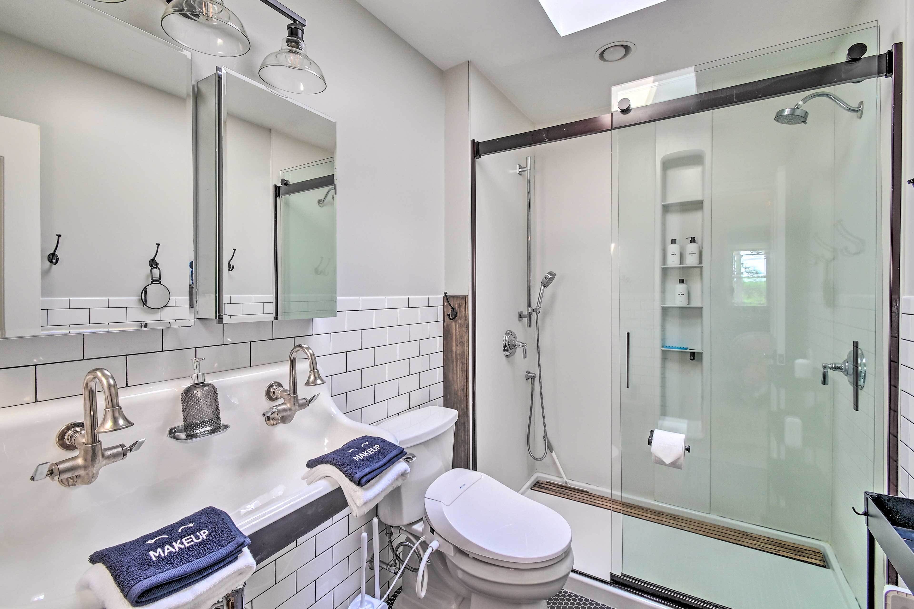 A modern bathroom with a glass-enclosed shower, a double sink with a towel, and a toilet.