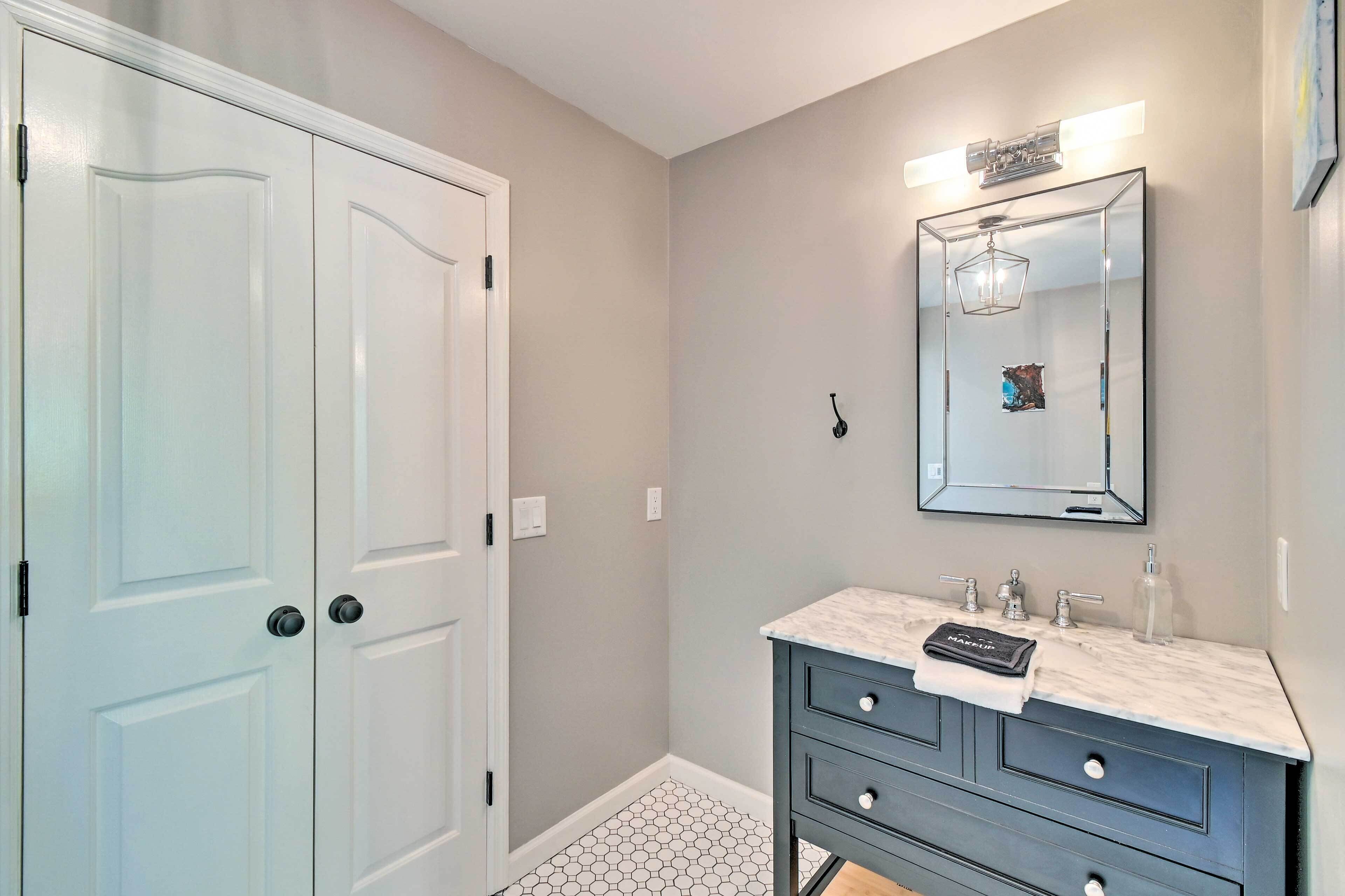A bathroom with a white door, a vanity with a mirror, and a hexagonal tiled floor.