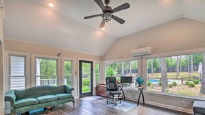 A spacious room with a green sofa, a black office chair, and a large window overlooking a backyard with a pool. - Peaceful Southern Pines Home w/ Pool + Yard! (Southern Pines)