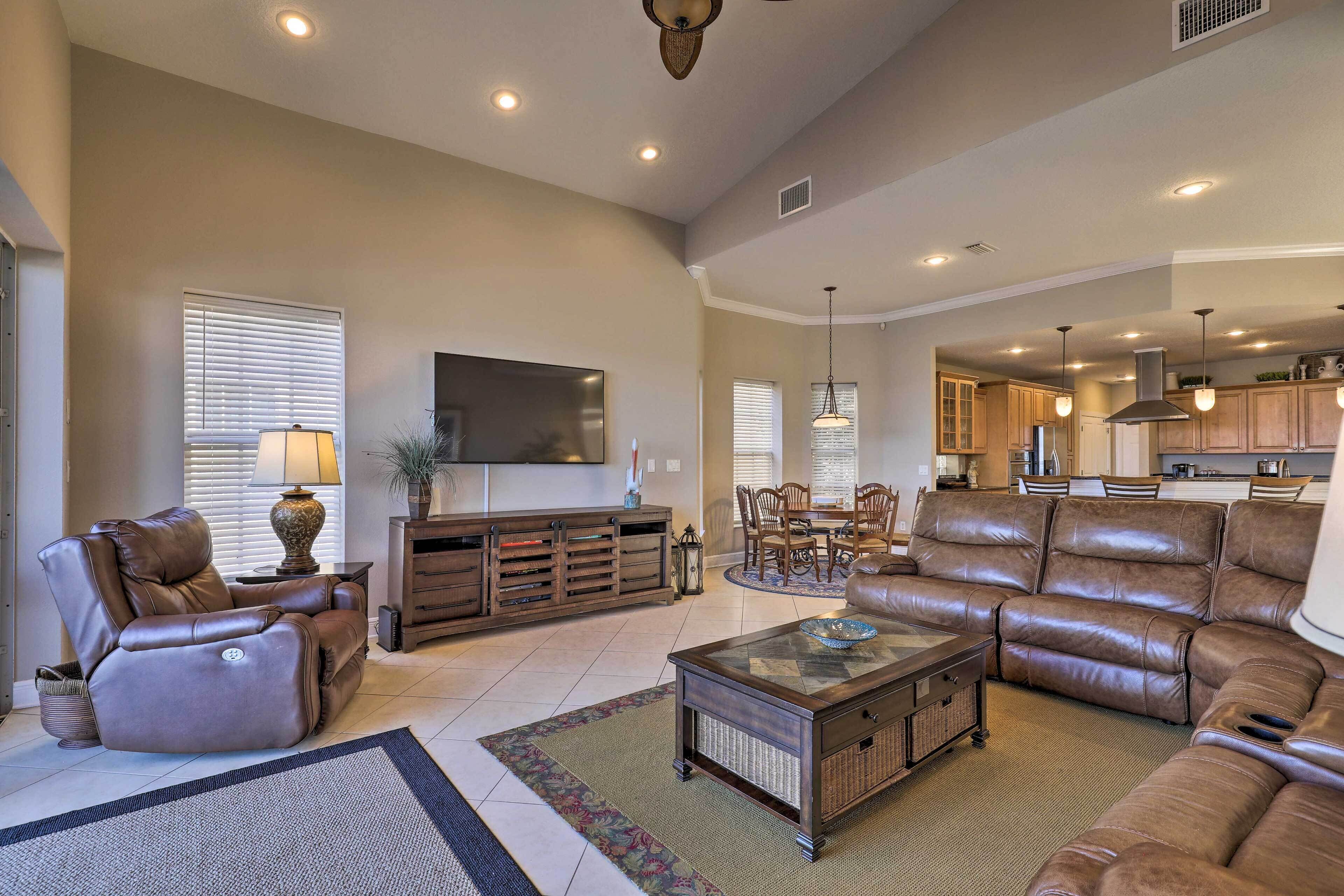 A spacious living room with a large leather sofa, a coffee table, and a flat-screen TV mounted on the wall.