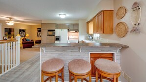 A modern kitchen with a central island, wooden bar stools, and decorative woven baskets on the wall.