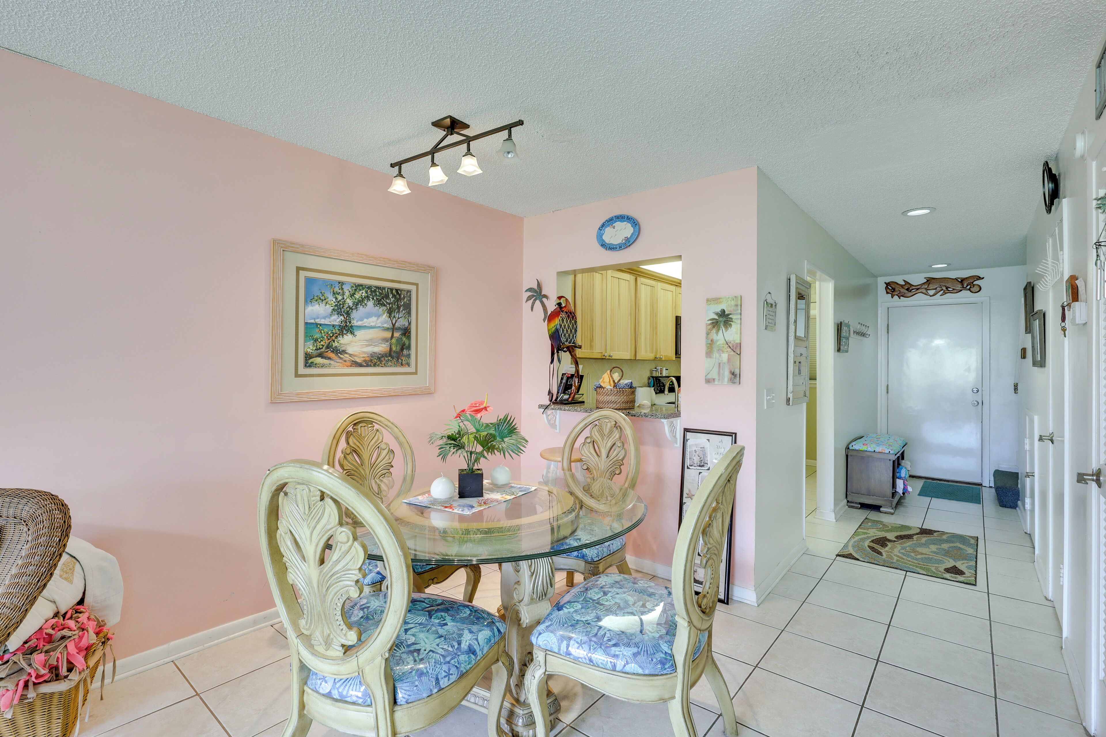 A dining area with a glass table surrounded by chairs, a painting on the wall, and a kitchen in the background.
