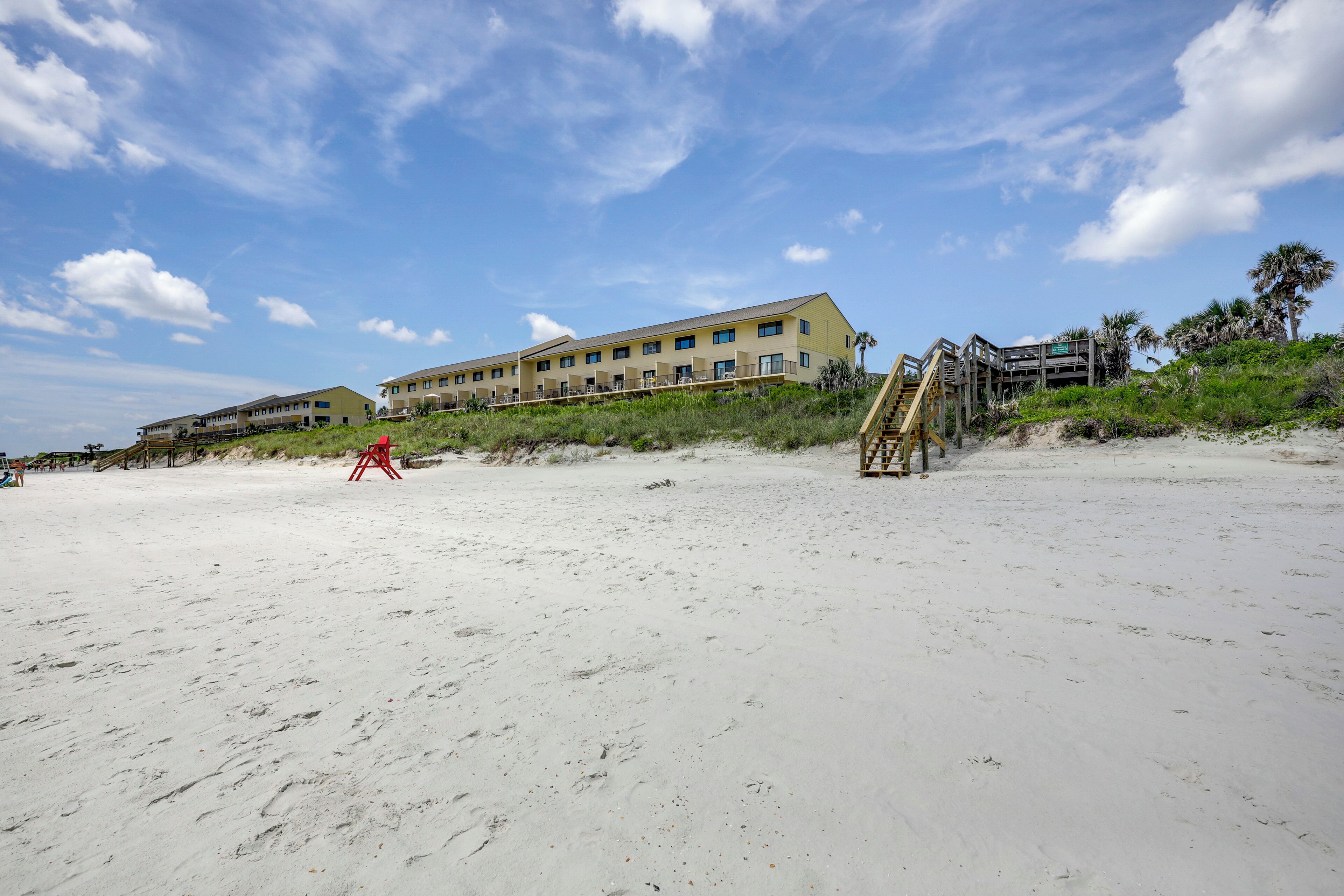 A beachfront hotel with multiple buildings, a sandy beach, and a staircase leading to the beach.