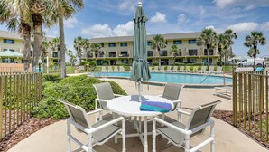 Un espace aménagé au bord de la piscine, avec une table ronde et des chaises, un parasol vert et une piscine.