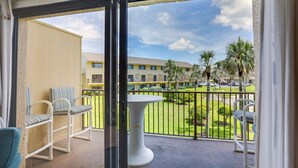 Un balcon avec une table et des chaises blanches, donnant sur une pelouse bien entretenue et un immeuble doté de nombreuses fenêtres.
