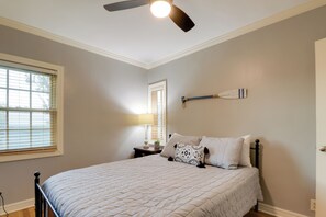 Une chambre à coucher comprenant un lit, un ventilateur de plafond, une table de chevet avec une lampe et une étagère fixée au mur.