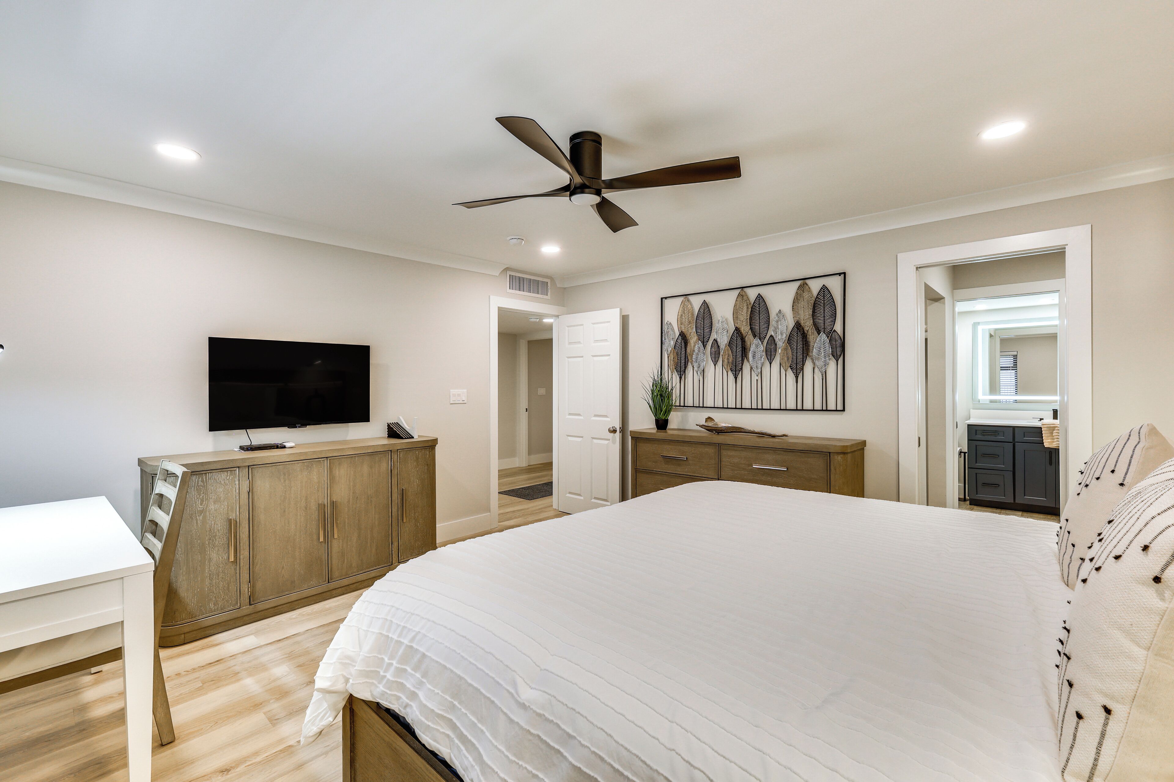 Una camera da letto con un letto grande, una televisione, una ventola a soffitto e un comò in legno.
