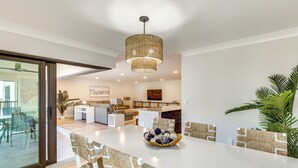 Een moderne keuken met witte kastjes, een centraal eiland en een eethoek met een witte tafel en geweven stoelen.