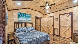 A wooden cabin bedroom with a bed, a ceiling fan, and wooden doors. - Somerset Cabin, Close to Lake Access! (Somerset)