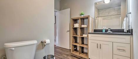A bathroom with a toilet, a wooden shelf with towels, a mirror, and a sink with a countertop.
