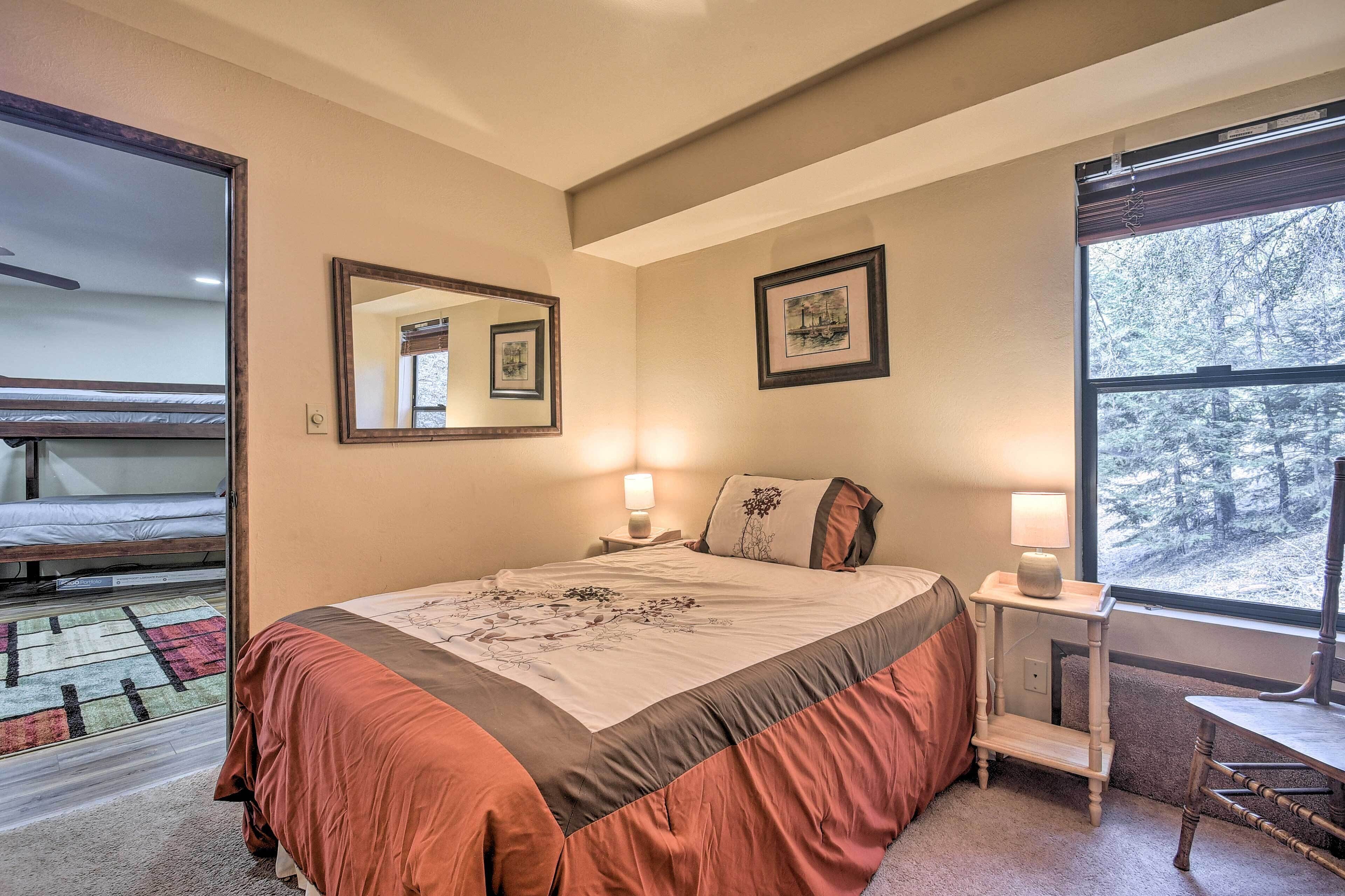 A bedroom with a bed, bedside tables, a window with a view of trees, and a mirror on the wall.
