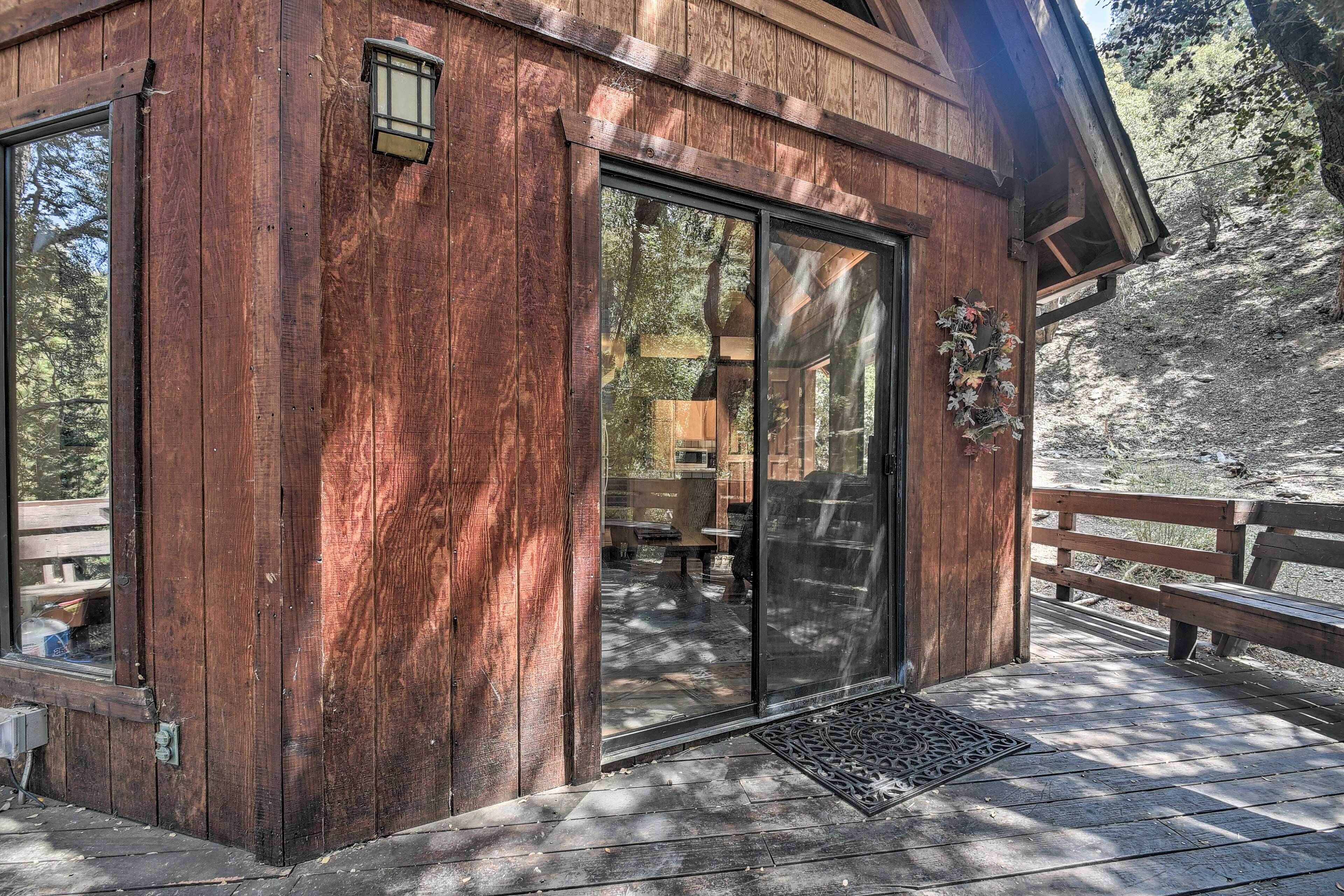 A wooden cabin with large sliding glass doors, a wooden deck, and a bench.