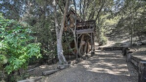 A treehouse with a wooden deck and a staircase leading up to it, surrounded by dense forest. - Updated 'tree House' Pine Mtn Club Cabin by Trails (Pine Mountain Club)