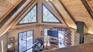 A wooden interior with a large window, a television, and a bookshelf. - Updated 'tree House' Pine Mtn Club Cabin by Trails (Pine Mountain Club)