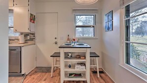 A compact kitchen with a built-in dishwasher, a small island with shelves, and a window providing a view of the outdoors. - Couples Getaway in North End Boise - Walk to Dtwn (Boise)