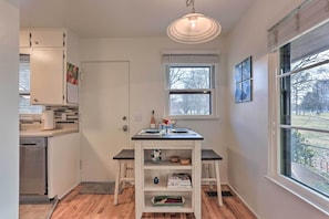 A compact kitchen with a built-in dishwasher, a small island with shelves, and a window providing a view of the outdoors. - Couples Getaway in North End Boise - Walk to Dtwn (Boise)