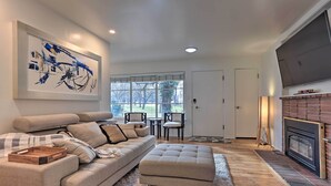 A modern living room with a sofa, ottoman, and a fireplace. There is a large painting on the wall and a TV mounted above the fireplace. - Couples Getaway in North End Boise - Walk to Dtwn (Boise)