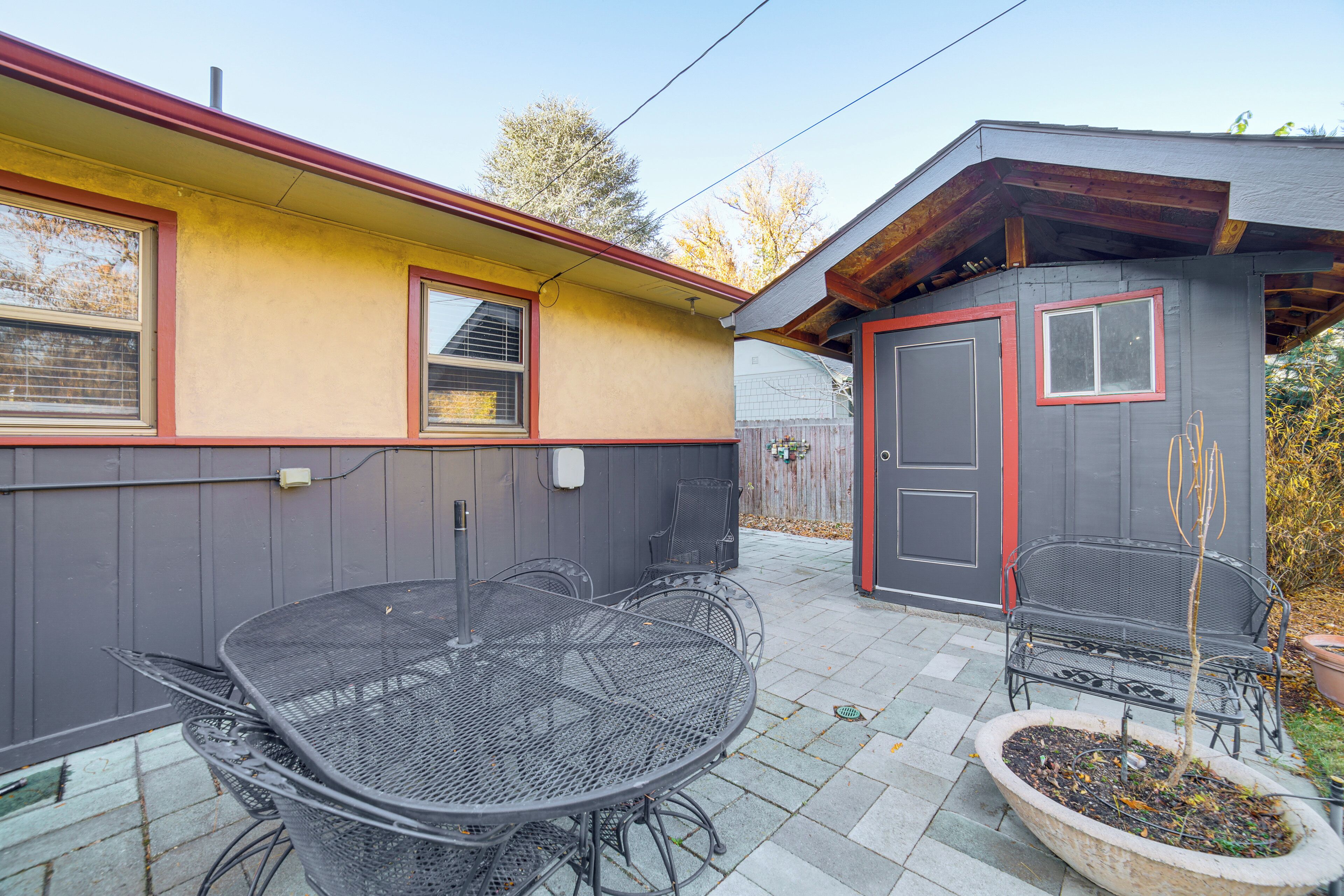 A patio with a metal table and chairs, a small shed, and a potted plant.