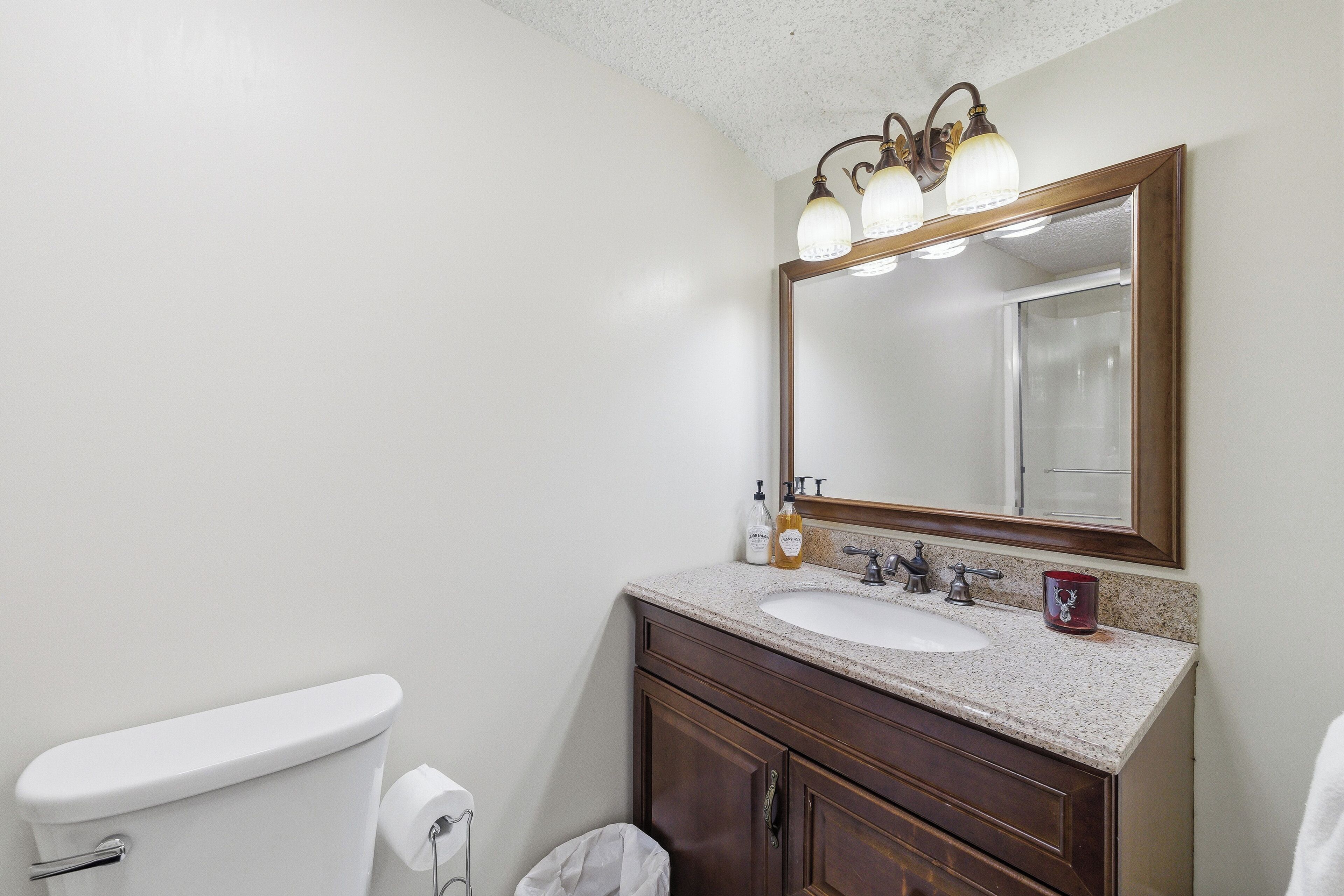 A bathroom with a white toilet, a sink with a mirror above it, and a trash bin.