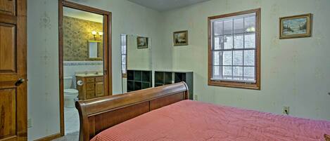 A bedroom with a wooden bed, a ceiling fan, a window with blinds, and a door leading to a bathroom.