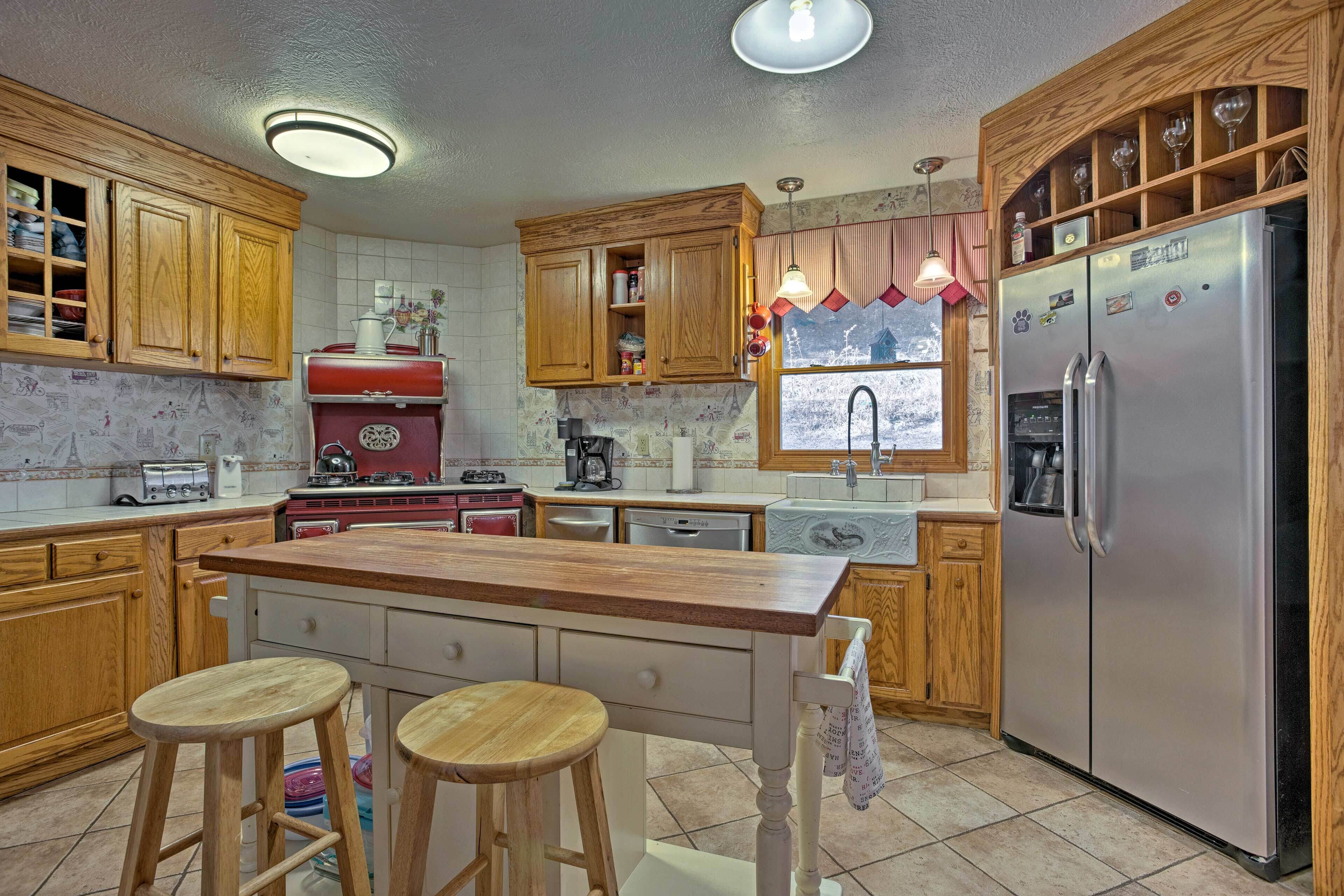A kitchen with wooden cabinets, a stainless steel refrigerator, a red stove, and two stools.