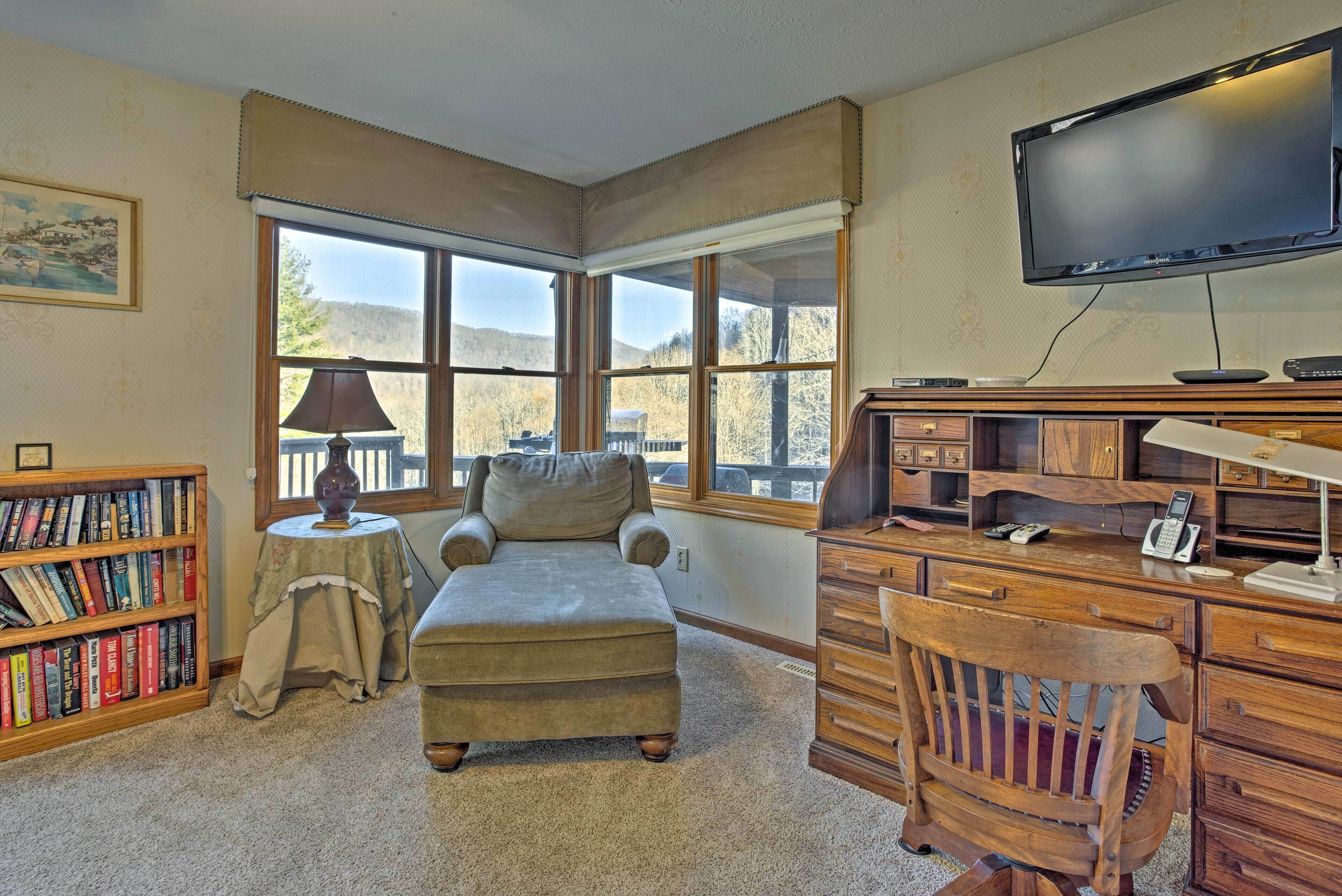 A cozy room with a large window, a comfortable armchair, a wooden desk with a telephone, and a bookshelf filled with books.