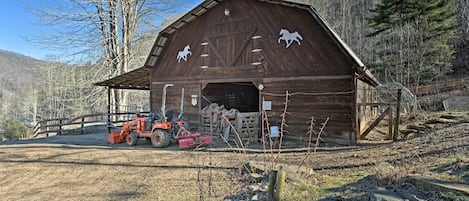 A wooden barn with horse silhouettes on the side, a tractor parked in front, and a clear sky.