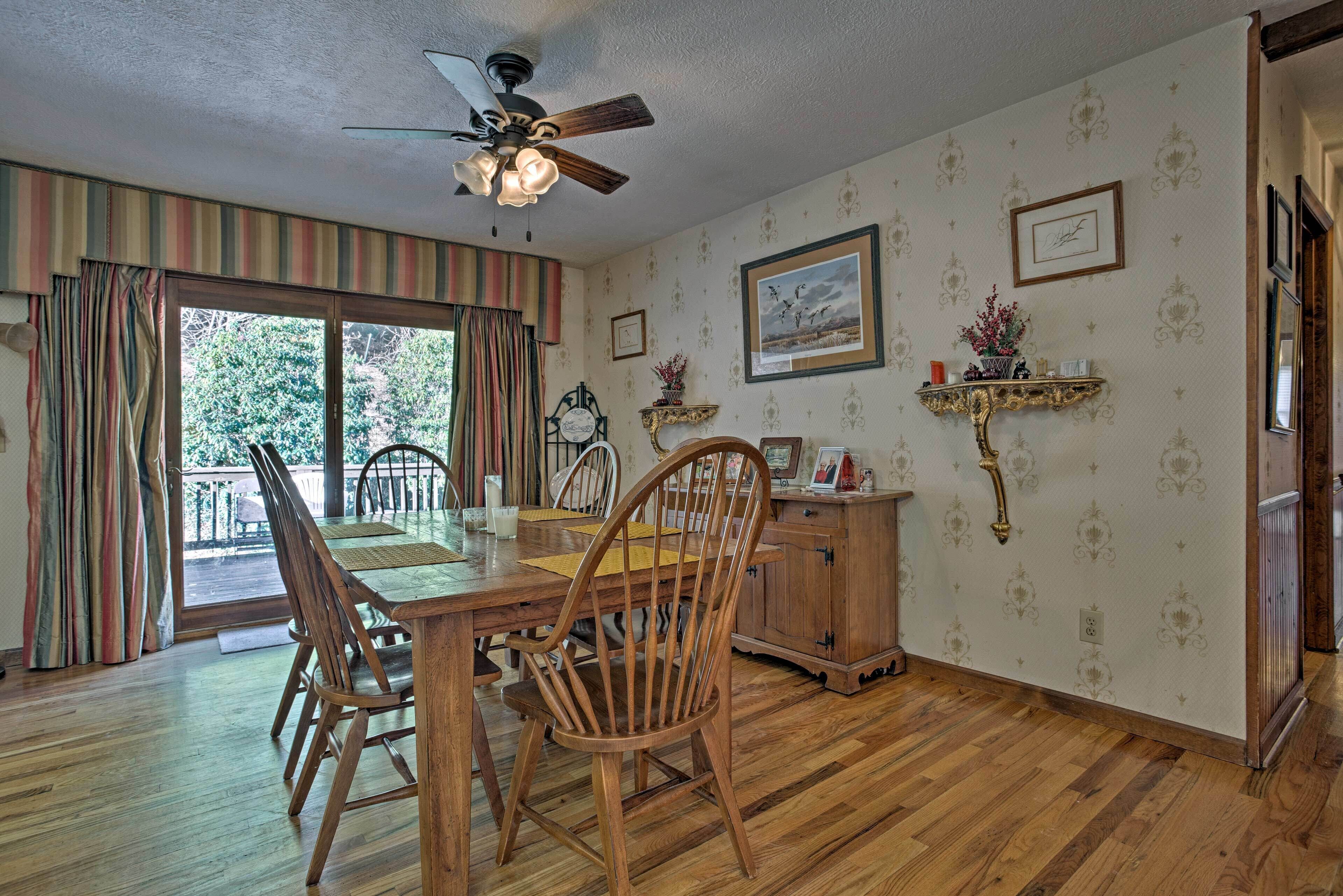 A dining area with a wooden table and chairs, a ceiling fan, and a view through a glass door to the outdoors.