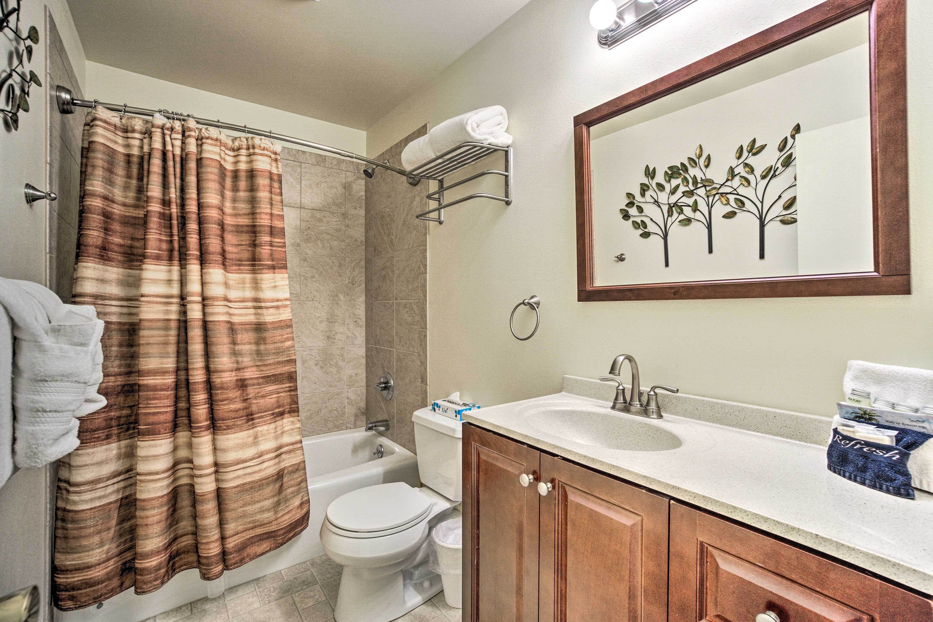 A bathroom with a shower curtain, toilet, sink, and cabinet.