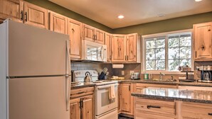Une cuisine avec des meubles en bois, un réfrigérateur, une cuisinière et une fenêtre donnant sur les arbres.